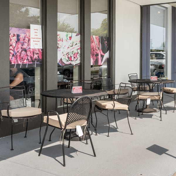Outdoor patio with black wrought iron tables and cushioned chairs outside Simply Delicious Restaurant.