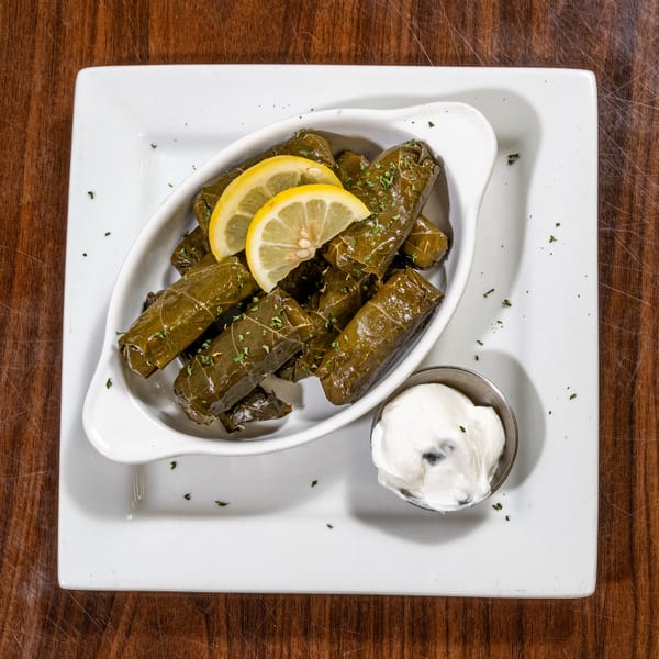 Stuffed grape leaves with lemon and herbs, served with a side of white sauce.