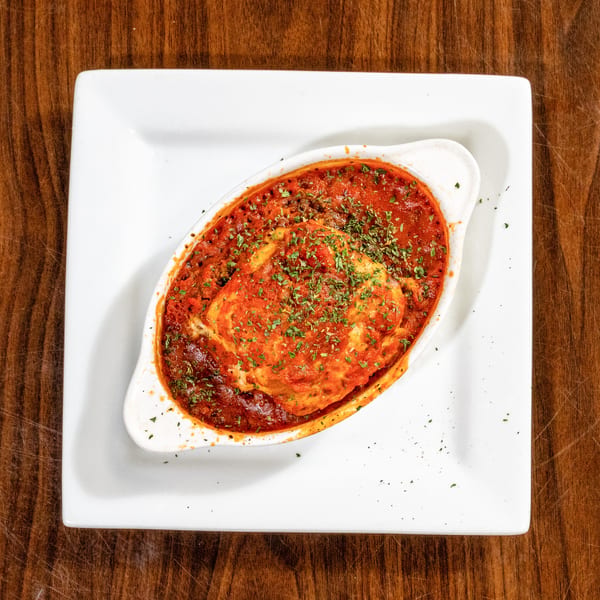 Baked pasta dish with rich red sauce and green herbs in a white oval bowl.