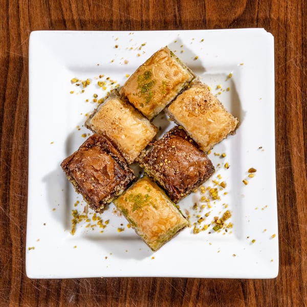 Overhead view of six assorted baklava pieces on a white plate, sprinkled with nuts.