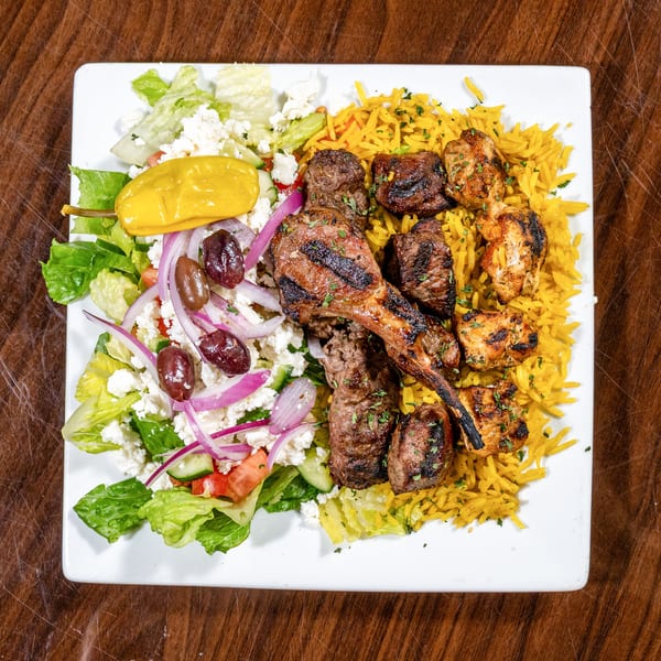Plate with grilled lamb chop, chicken and beef kebabs, yellow rice, and a Greek salad.