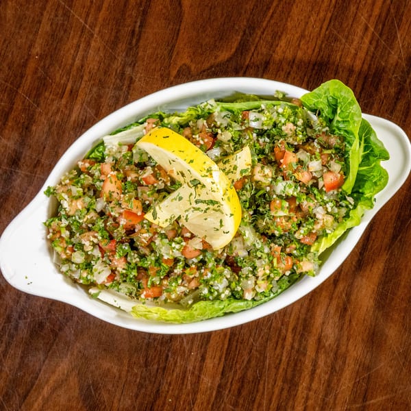 Tabbouleh salad in a white dish, garnished with lemon wedges and lettuce, on a wooden surface.