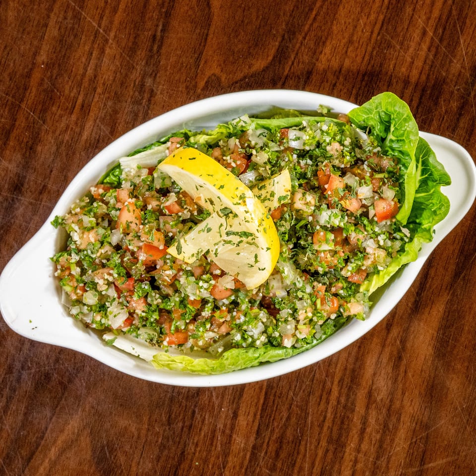Tabbouleh salad in a white dish, garnished with lemon wedges and lettuce, on a wooden table.